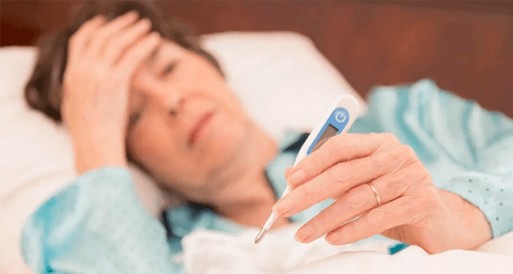 Mulher deitada na cama com febre e segurando um termômetro - Coronavírus