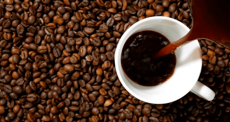 Café sendo derramado em uma xícara com mesa coberta de grãos de café